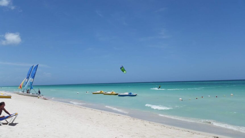 A beautiful beach near Havana with clear turquoise waters, white sandy shores, and palm trees. People are sunbathing, swimming, and enjoying various beach activities, reflecting the perfect coastal escape.